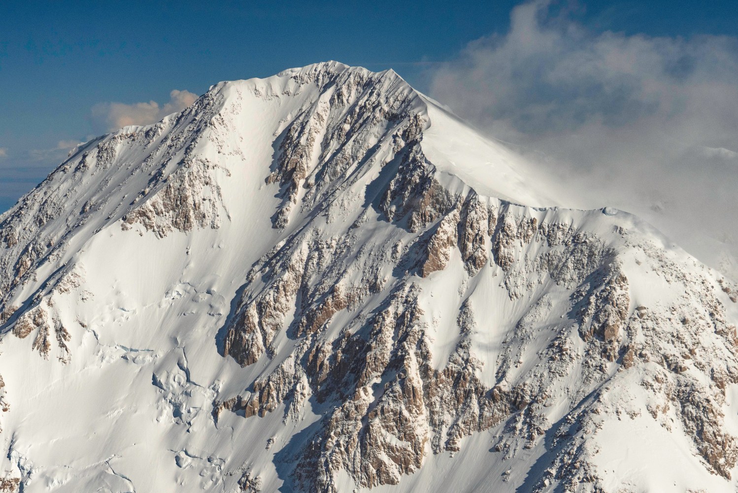 Snow-covered Denali with rocky ridges under a clear blue sky.