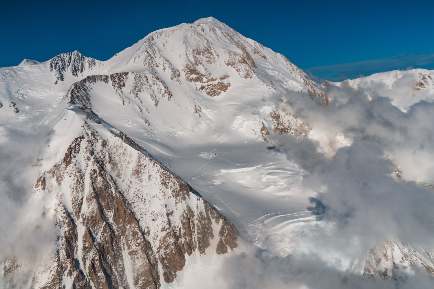 Snow-covered mountain peak with clouds and blue sky backdrop.
