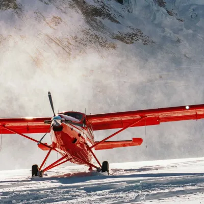 Red plane on snowy terrain with mountains in the background under a clear sky.