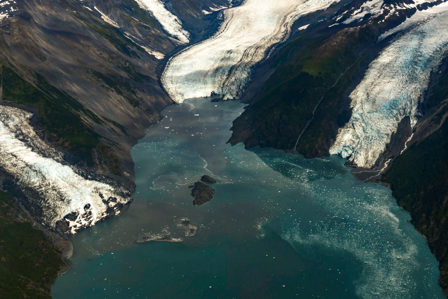 Aerial view of a turquoise fjord surrounded by glaciers and mountains.