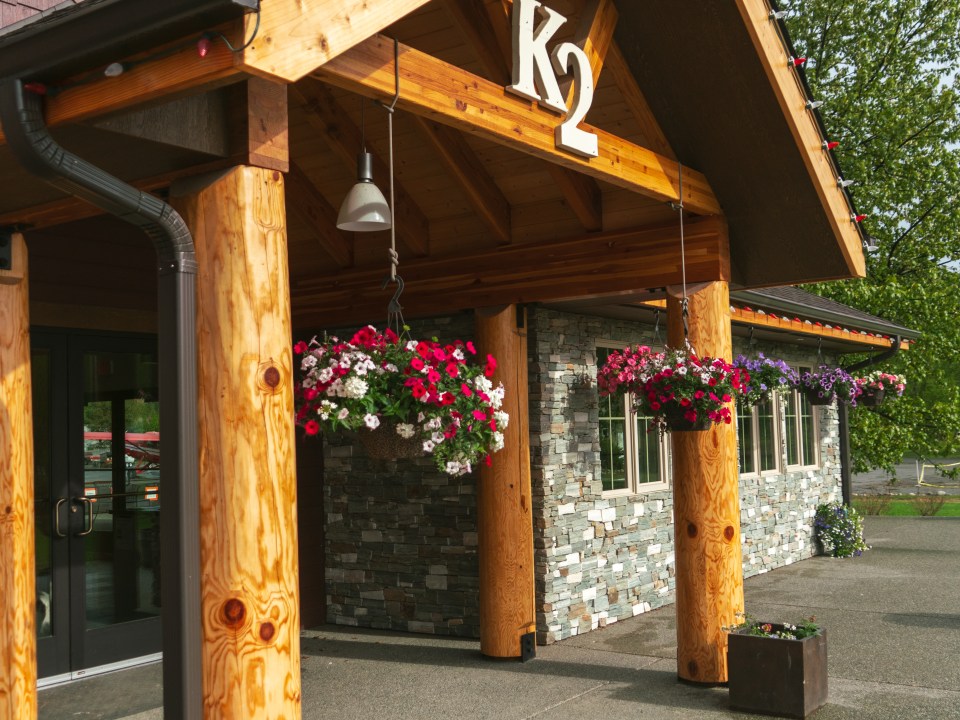 Wooden building entrance with hanging flower baskets and stone wall.