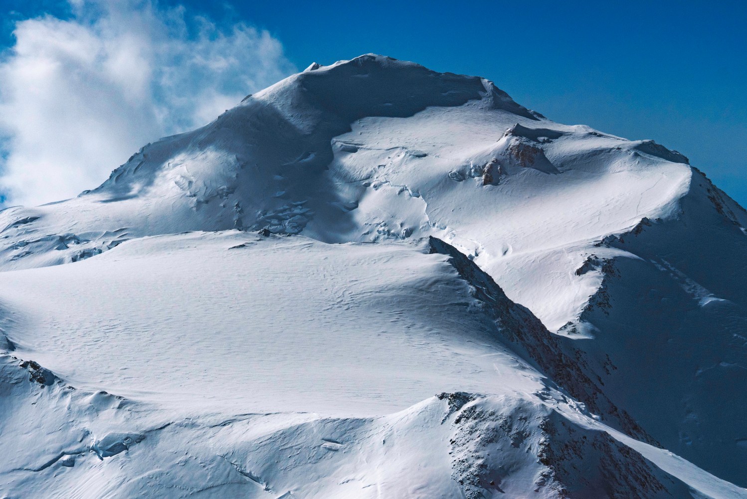 Snow-covered mountain peak under a clear blue sky with some clouds.