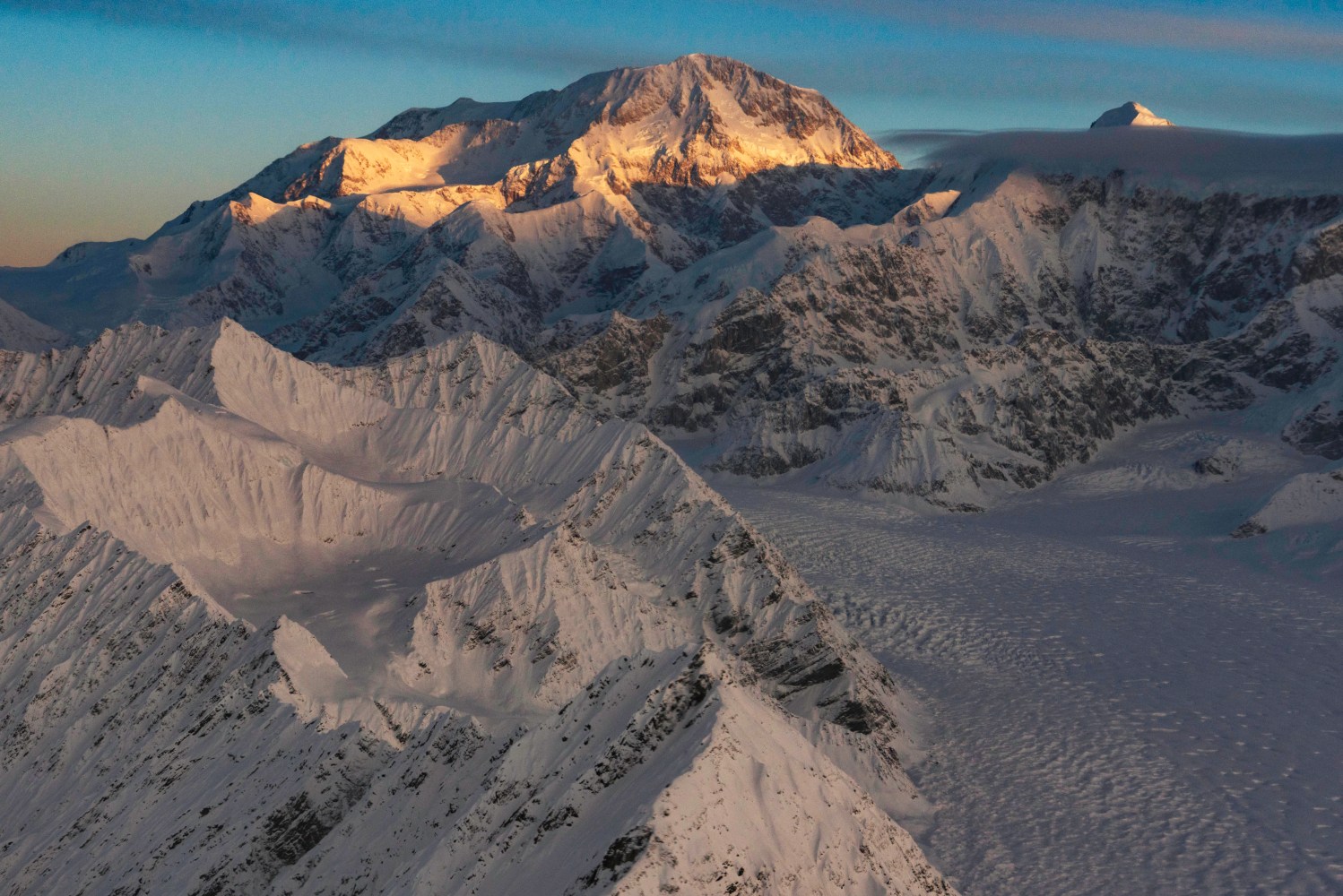 Snowy mountain range at sunset with glowing peaks and shadowed valleys.