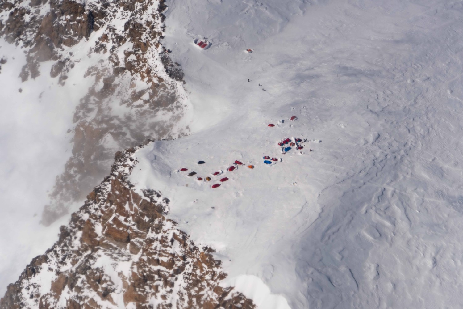 Aerial view of a snowy mountain with colorful tents scattered on a flat area in Denali National Park