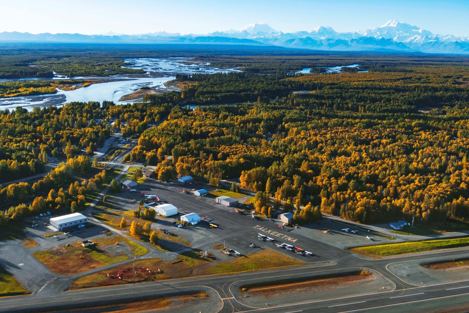 Aerial view of Talkeetna runway surrounded by forest with the Alaska Range including Denali in the background