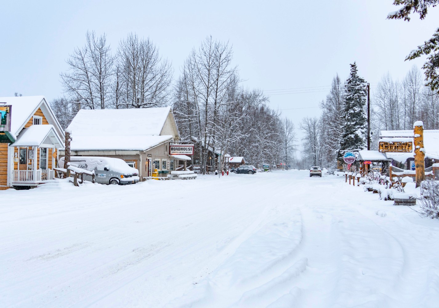 Snow-covered Main Street in Talkeetna Alaska with shops and cars in winter landscape.
