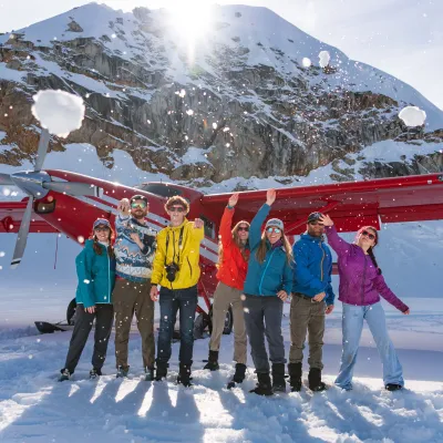 Group of people throwing snowballs in front of a red small plane on a snowy mountain.