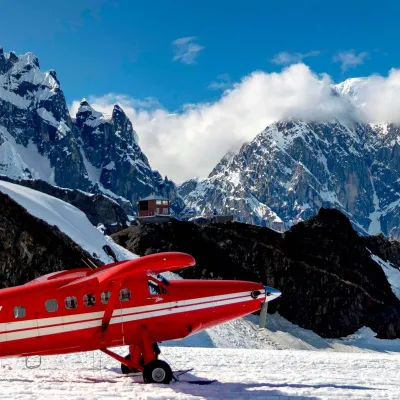 Red air taxi plane on snowy mountain landscape with clear blue sky and rugged peaks in the background.
