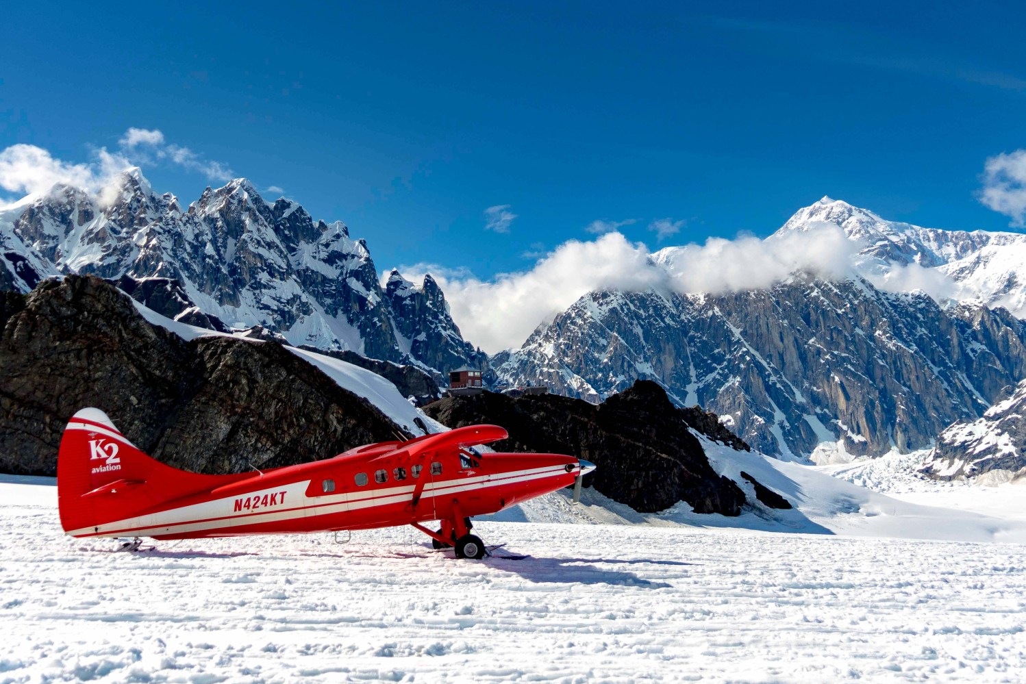 Red air taxi plane on snowy mountain landscape with clear blue sky and rugged peaks in the background.