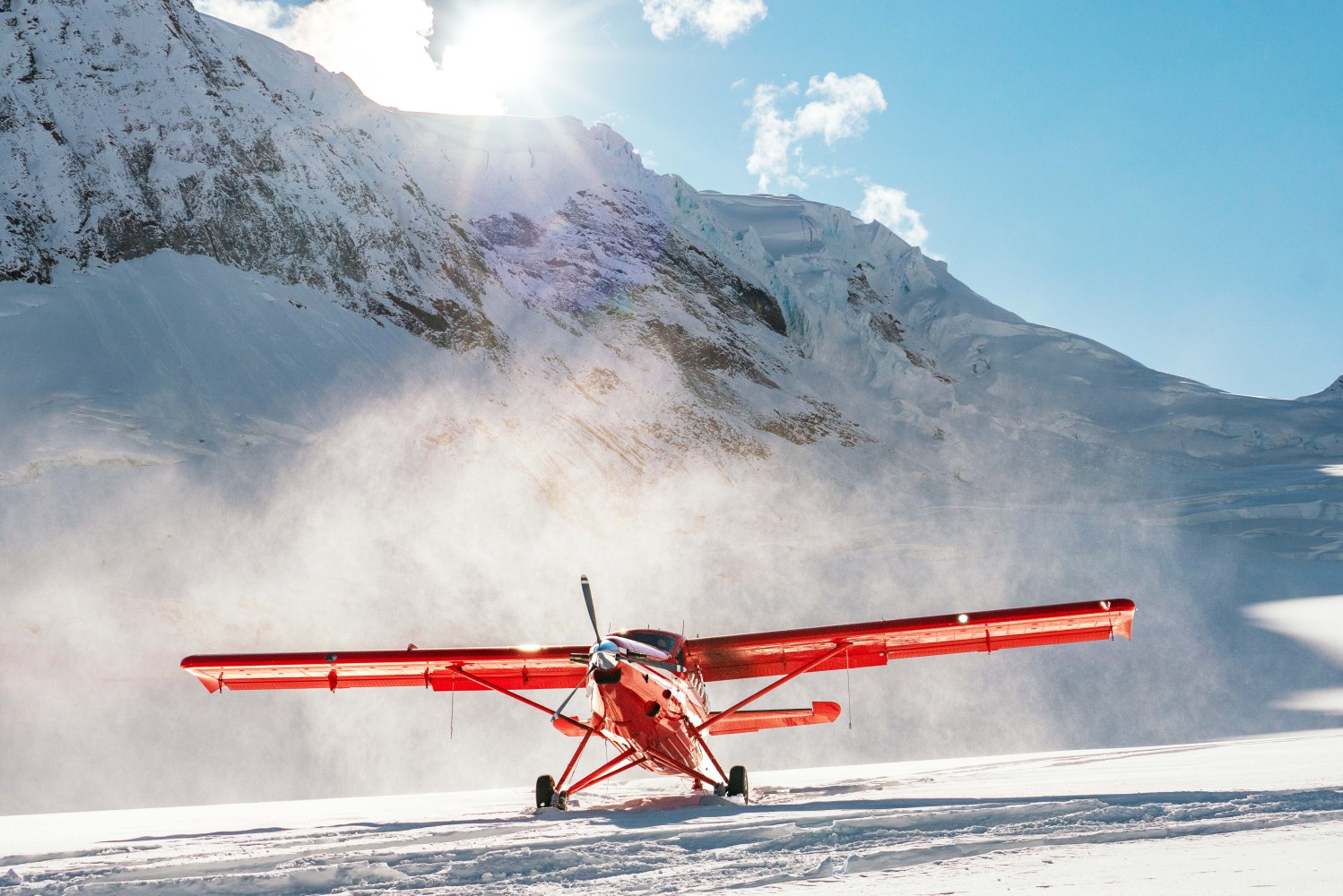 Red air taxi plane on snowy mountain landscape with sun shining.