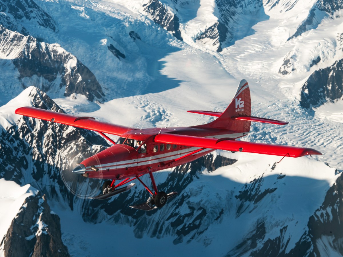 Red airplane flying over snow-covered mountains and glaciers.