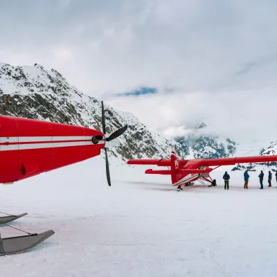 Red planes on snowy mountains, with people standing nearby.